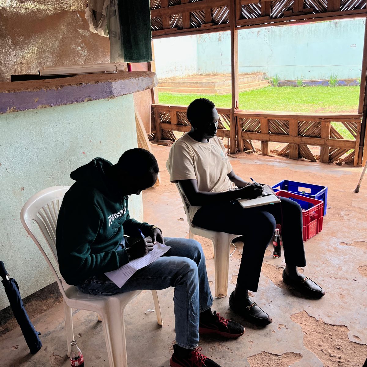 Two young men write in their notebooks during a workshop in Kiryandongo Refugee Settlement