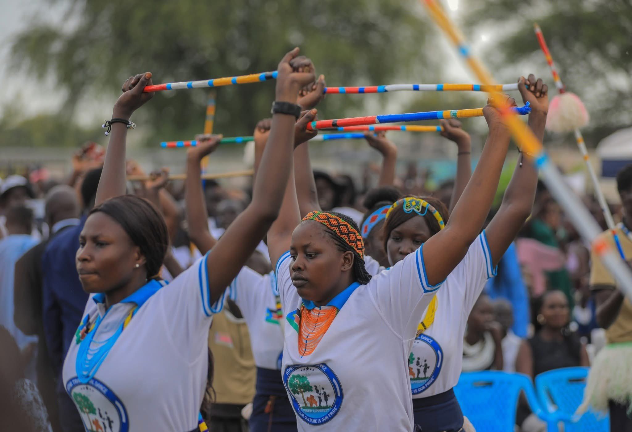 Young women in matching white shirts raise brightly beaded sticks overhead together during a dance at Peace Cultural Day